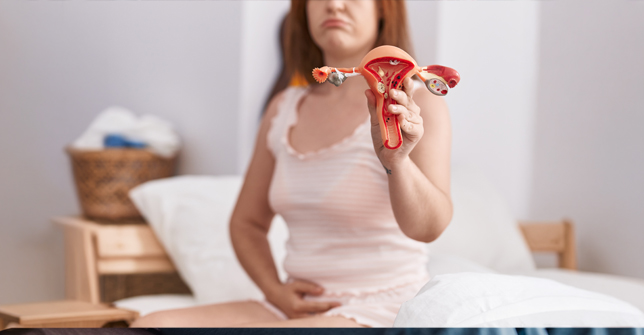 Woman in loungewear holding a model of female reproductive organs, illustrating polyendocrine metabolic ovarian syndrome (PMOS).