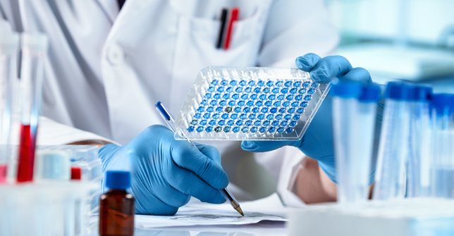A scientist in a lab coat holds a blue microplate while conducting preimplantation genetic testing.