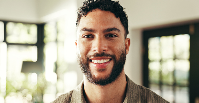 Smiling man with curly hair and a beard, representing male fertility and wellness in a bright, inviting setting.