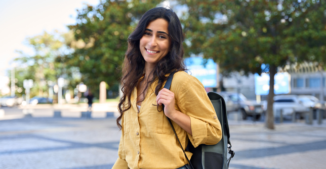 Smiling woman in a yellow shirt with a backpack stands outdoors, symbolizing resilience and empowerment in managing pelvic pain.
