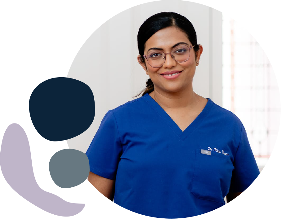 A smiling woman with dark hair and glasses wears a blue V-neck medical scrub top with a name tag reading Dr. Rita Dutta in a circular portrait.